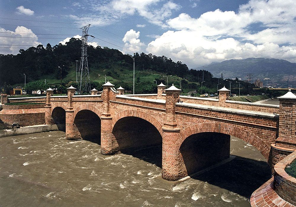el Puente de Guayaquil. Construido entre 1877 y 1879, este puente carretero no solo conecta físicamente las orillas del río Medellín, sino que también une siglos de historia, cultura y desarrollo urbano